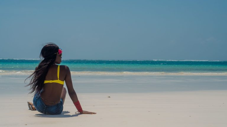 Woman standing on the white sand of Diani Beach, Kenya, looking out over the turquoise Indian Ocean