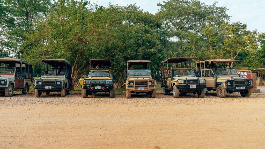 A row of different open-sided safari 4x4 vehicles parked side by side on a dirt track