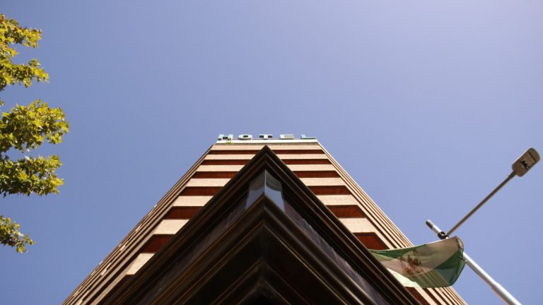 Low-angle view of a modest multi-storey hotel building along a highway in Kenya, under a clear blue sky