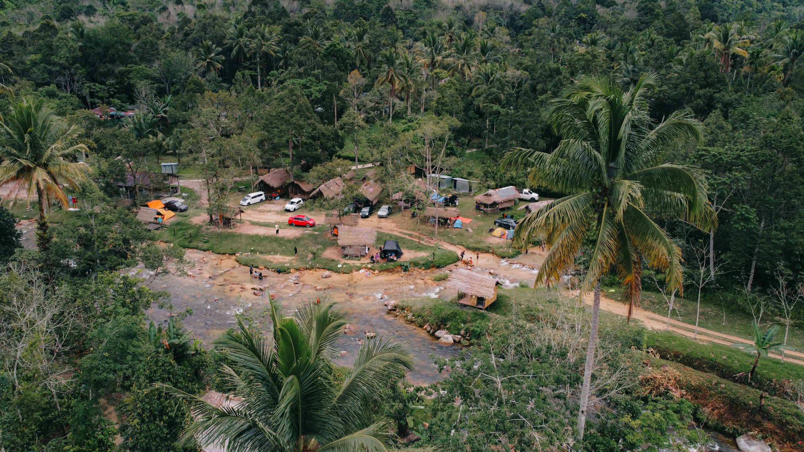 Aerial view of a riverside tented camp with palm trees along the water