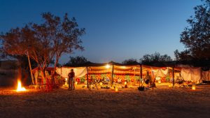 Desert camp illuminated at dusk with a campfire glow