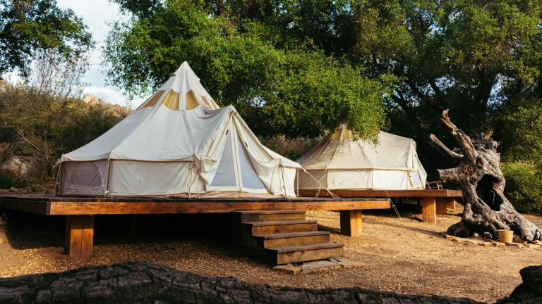 Two spacious canvas tents on a wooden platform in a serene forest setting