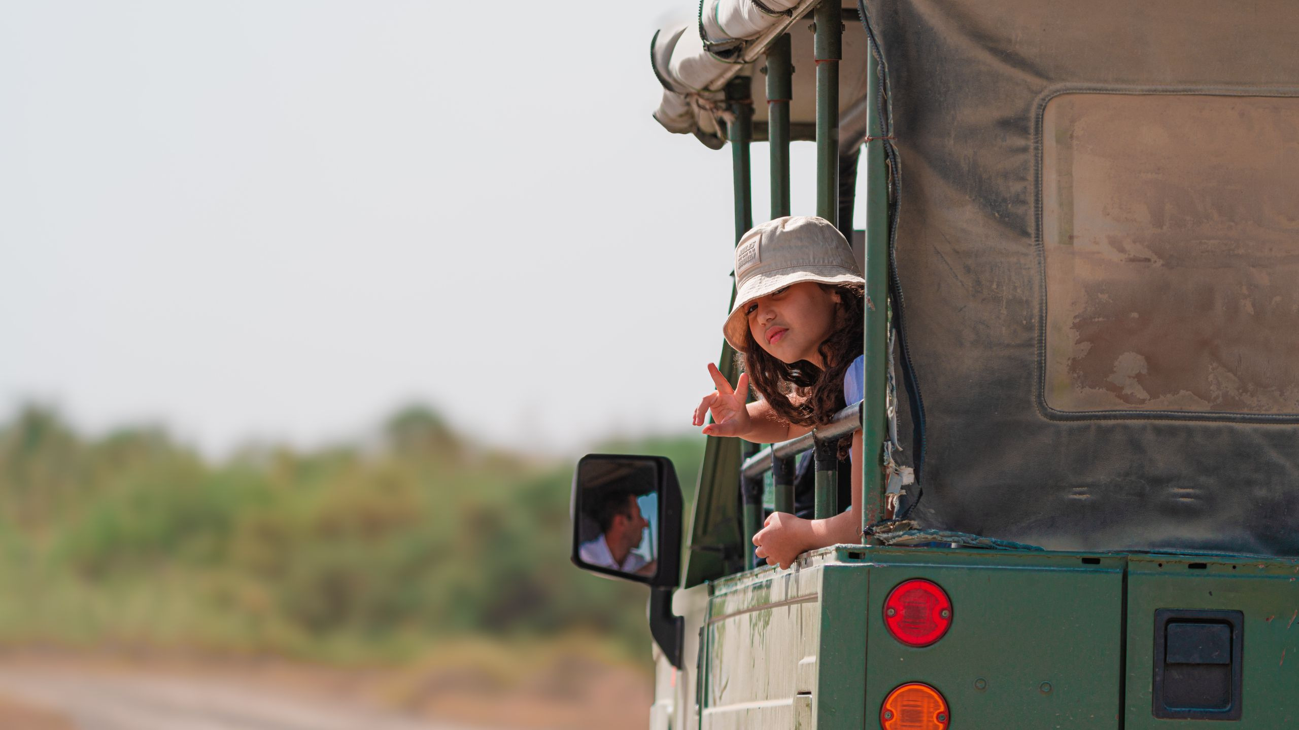 A young girl smiles while riding in an open-top safari vehicle through the wilderness